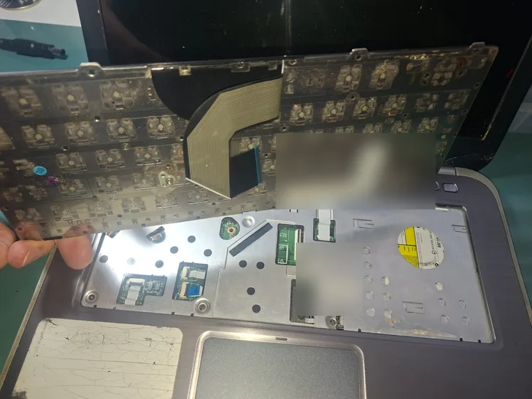 Teclado de notebook Dell sendo retirado, com o cabo flat ainda preso à placa