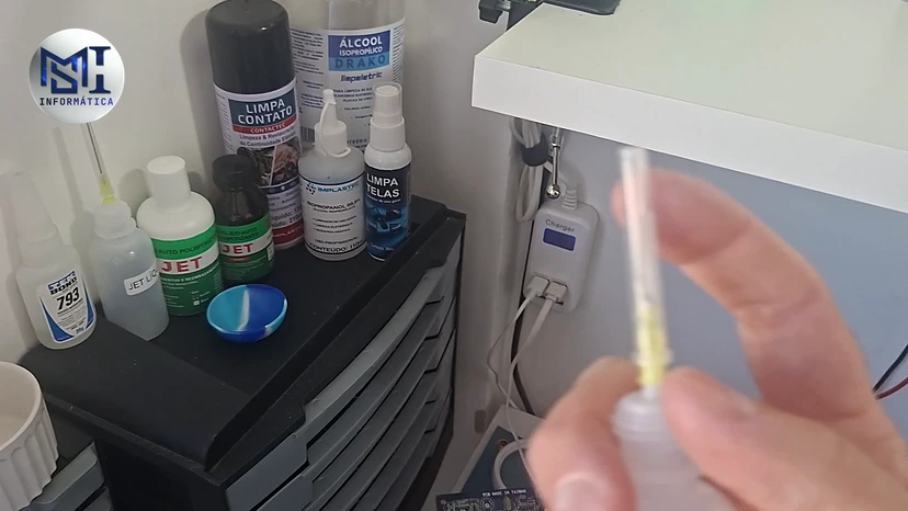 Frascos de álcool isopropílico, limpa contato e limpa telas na prateleira, com um frasco aplicador na mão, no vídeo do canal