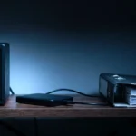 NAS de duas baias e um HD externo numa estante de escritório pequeno, ao lado de pastas de documentos
