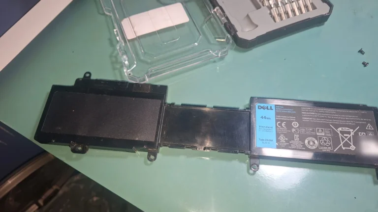 Bateria interna Dell de 44 Wh tirada de um notebook, em cima da mesa ao lado do kit de chaves; etiqueta de série desfocada