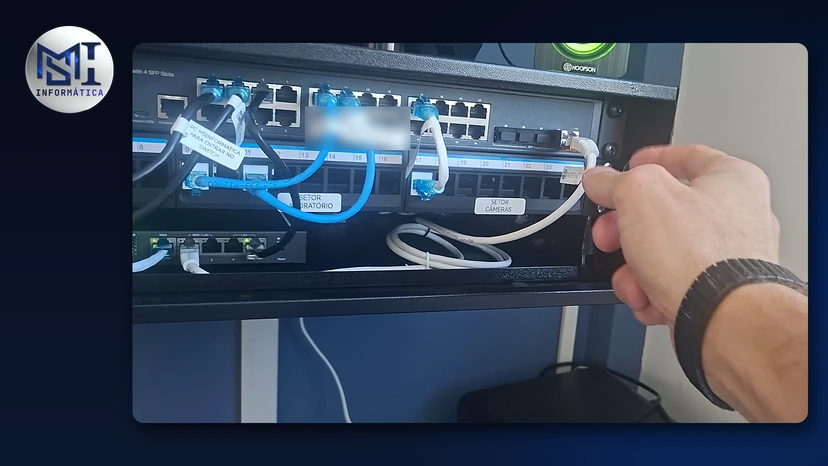 Mão do técnico ligando o cabo da internet no rack de rede do escritório da MSI, com switch e patch panel identificados por setor, no vídeo do canal