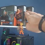 Mão do técnico nas caixas de placa-mãe B760M e H610M numa estante, acima de um PC gamer com water cooler aceso
