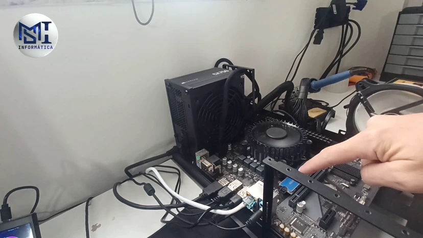 Dedo do técnico apontando o slot da placa-mãe montada fora do gabinete, antes de escolher o SSD, no vídeo do canal