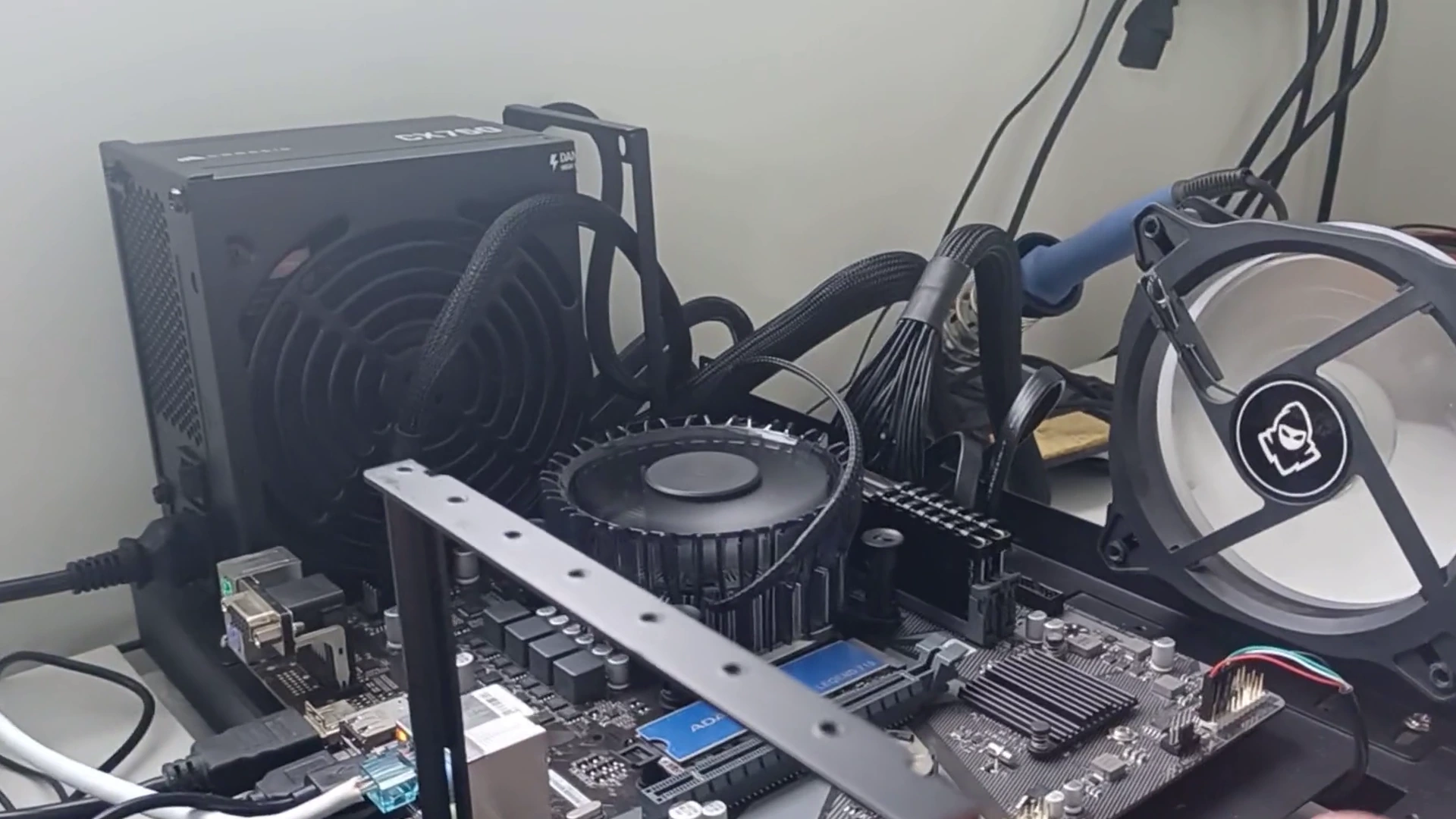 Cooler do processador montado na placa-mãe, numa estrutura de teste aberta com a fonte e uma ventoinha, no vídeo do canal sobre a temperatura da CPU