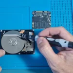 HD mecânico aberto com o prato à mostra e um SSD aberto ao lado, na mesa, no vídeo do canal sobre HD e SSD