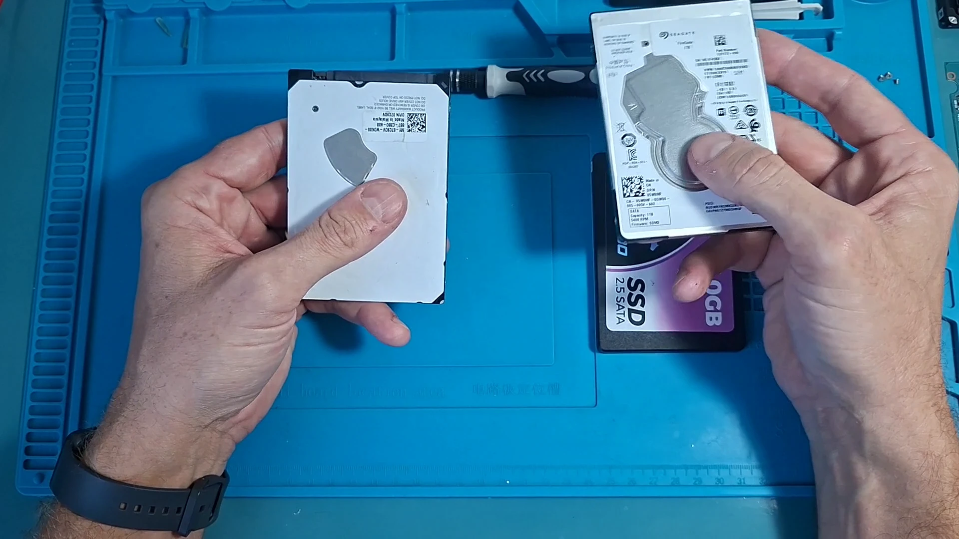 Dois HDs de notebook nas mãos do técnico e, embaixo, um SSD SATA de 2,5 polegadas