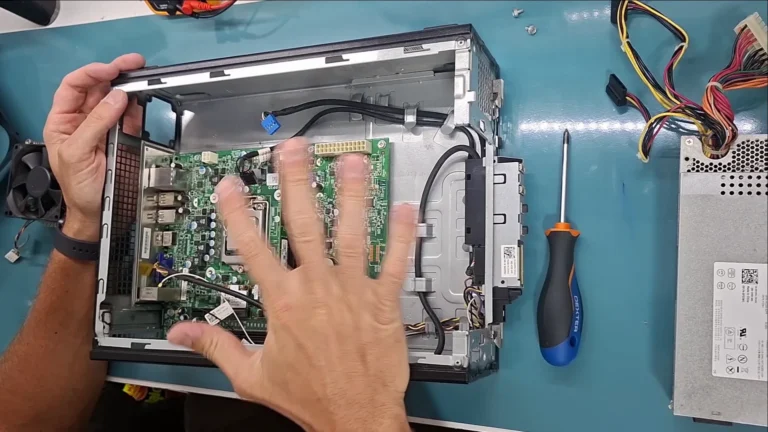 Mãos do técnico dentro de um Dell Vostro antigo aberto na mesa, durante o conserto, no vídeo do canal