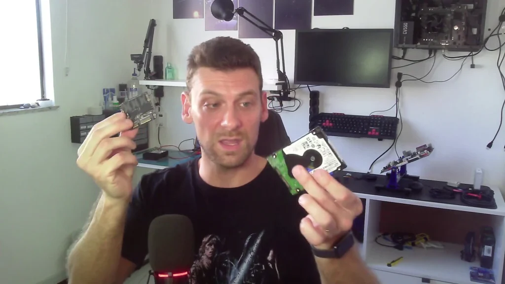 Marcello Di Silvestro segurando a placa de um SSD e um HD de notebook, no vídeo do canal