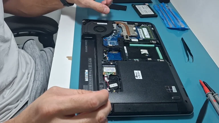 Mãos do técnico num notebook Lenovo aberto por baixo, com os slots de memória e a placa Wi-Fi à mostra