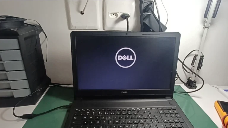 Notebook Dell aberto numa mesa com o logo da Dell na tela, ao lado do multímetro, no vídeo do canal