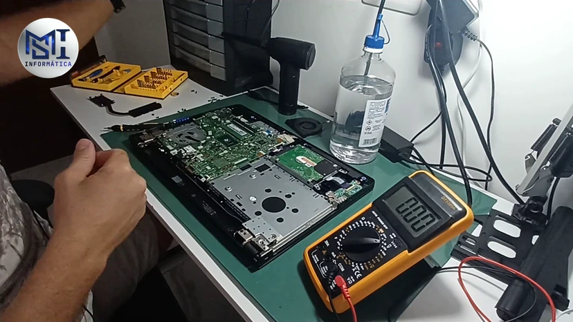 Notebook Dell desmontado na mesa, ao lado do multímetro, durante uma manutenção, no vídeo do canal