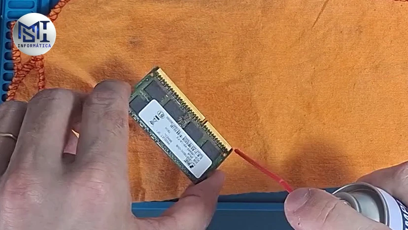 Pente de memória SO-DIMM de notebook na mão do técnico, recebendo spray limpa contato nos contatos dourados, no vídeo do canal