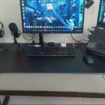 Setup do canal: mesa gamer preta com monitor LG, teclado mecânico com luz, mouse, headset no suporte, microfone e notebook