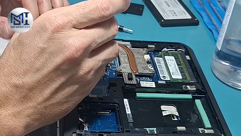 Mão do técnico no slot de memória de um notebook Lenovo aberto por baixo, durante a manutenção, no vídeo do canal