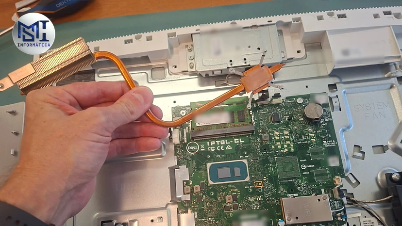 Mão tirando o conjunto de dissipador e heatpipe de um Dell All-in-One na manutenção, com a placa-mãe à mostra