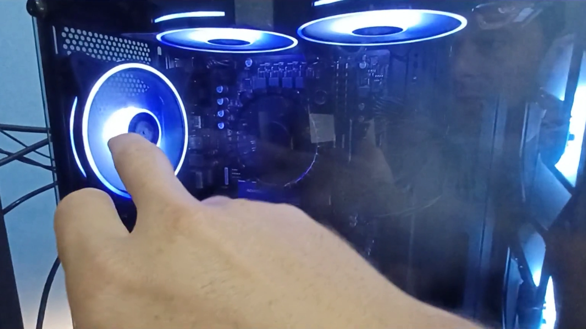 Dedo do técnico apontando a ventoinha traseira acesa de um PC gamer com ventoinhas azuis no topo